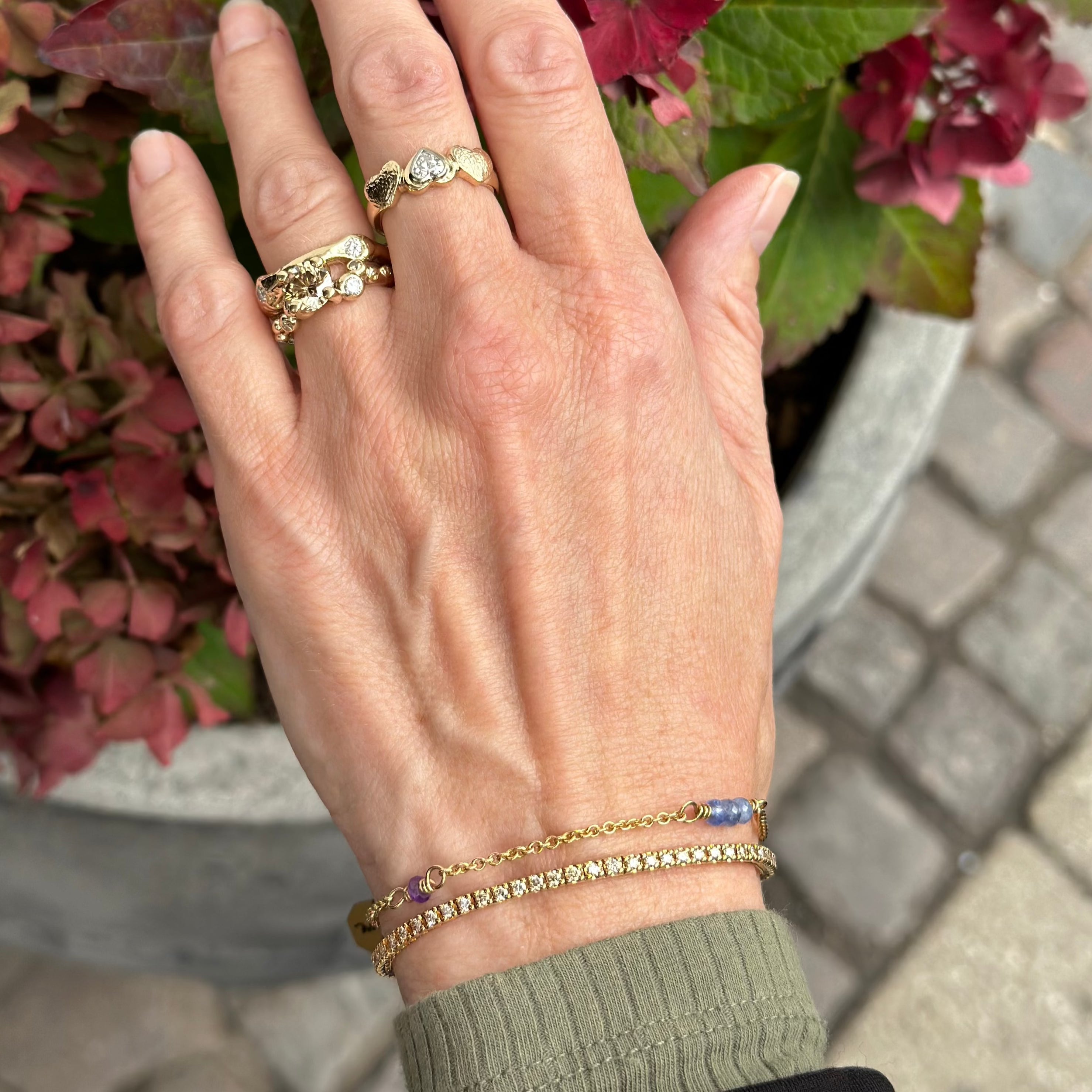 guldarmbånd med blå safir og ametys i fine snoninger. vises på kvindehånd sammen med et diamant armbånd