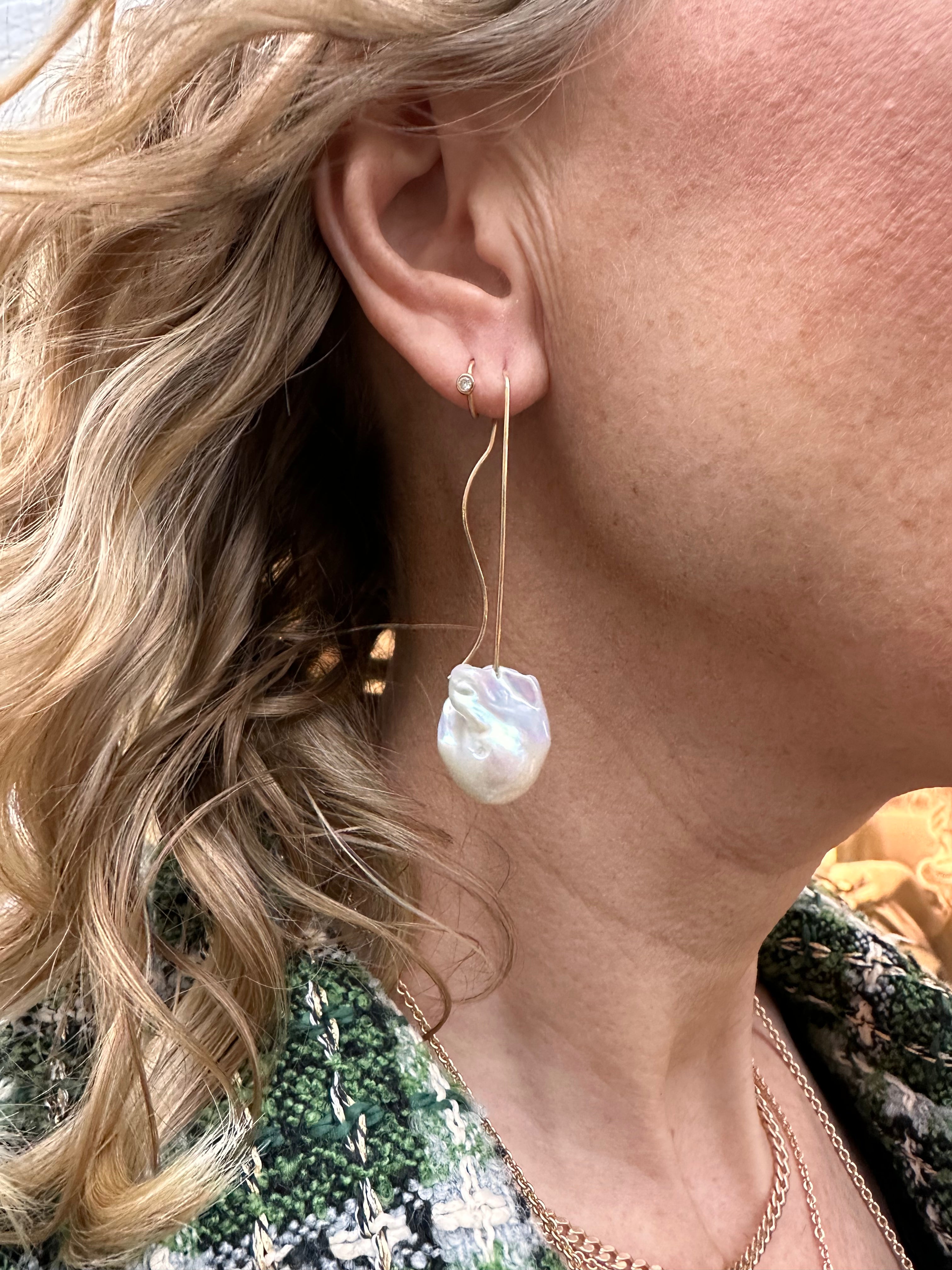14 kt. øreringe med barok ferskvandsperle Smukke og elegante øreringe, den fine guldbøjle svinger elegant på bagsiden af øret - en fin detalje der gør øreringen let og meget feminin. Perlerne er Hvide med let rosa skær, den barokke overflade gør perlerne mere levende og spændende i øret.