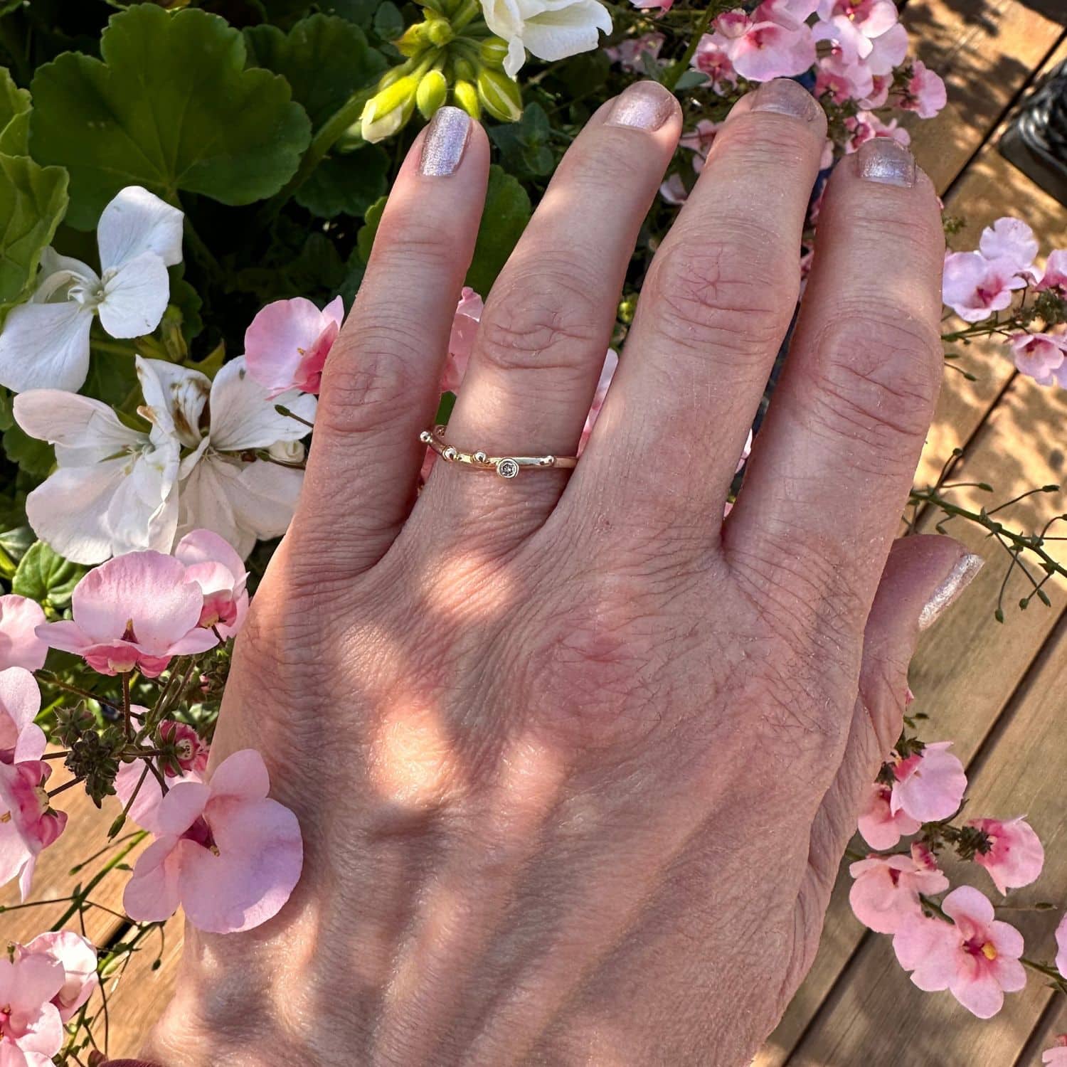 14 karat enekl guldring med guldkugler og en champagnefarvet brillant på 0,02 ct, båret på en hånd blandt lyserøde blomster.